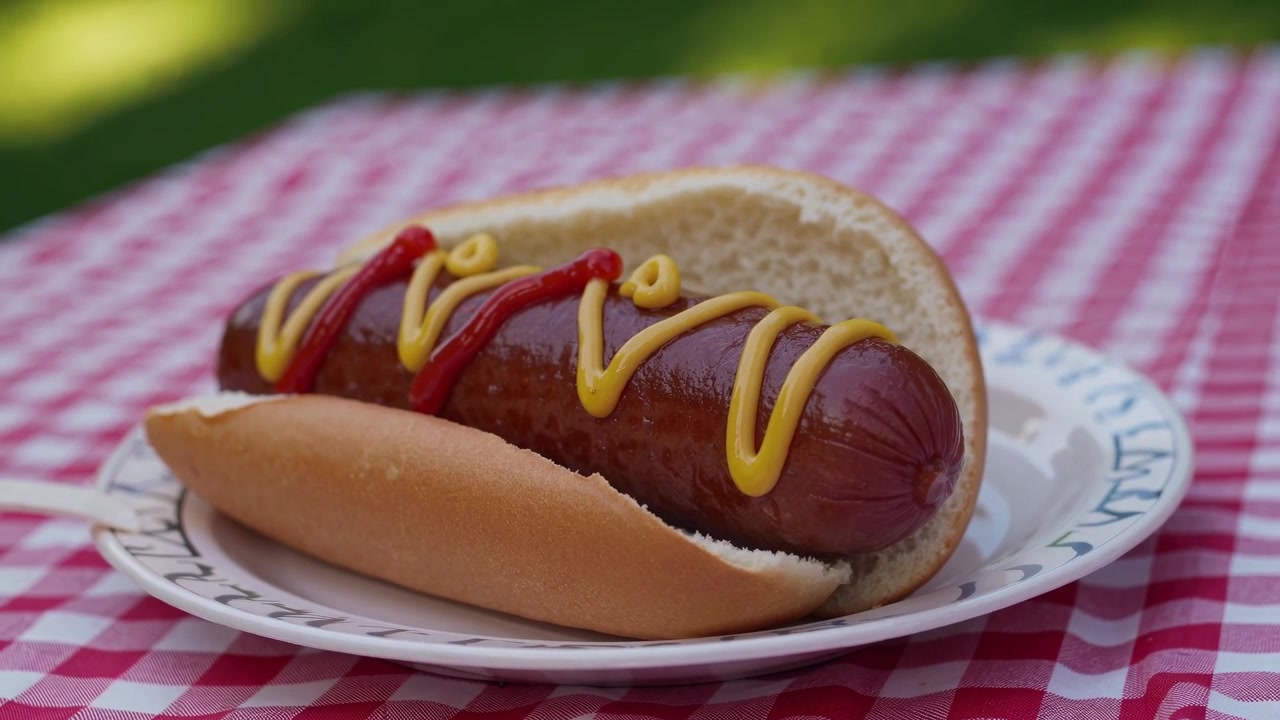 Detail hot dogu s kečupem a hořčicí na piknikovém stole.