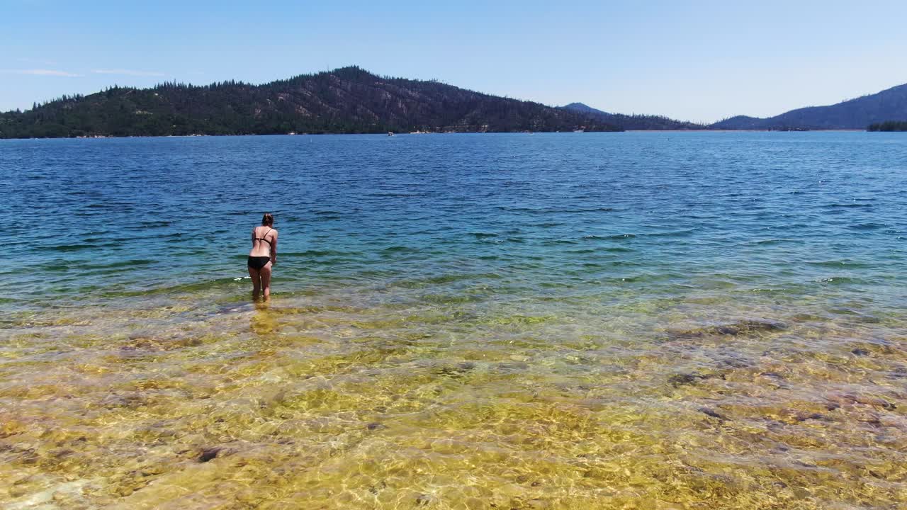 캘리포니아 의 위스키 타운 저수지 에 있는 푸른 소나무 로  ⁇ 인 산 들 의 배경 에 둘러싸여 있는 놀라운 파란 호수 에서 수영 하는 사람 을  ⁇ 처 한 드론 영상