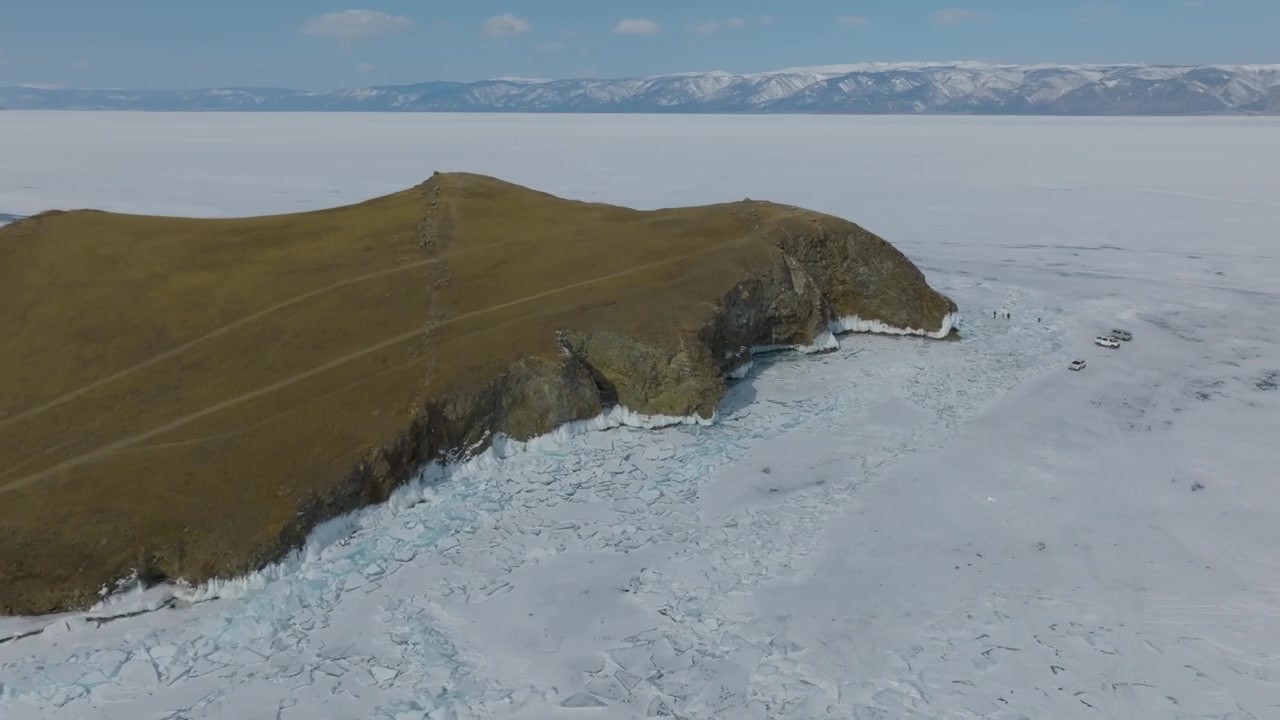 Droneoptagelse af Kharantsy-øen på den frosne Bajkalsø, med sne og mønstre af revnet is og fjerne bjerge under en klar blå himmel, Sibirien, Rusland
