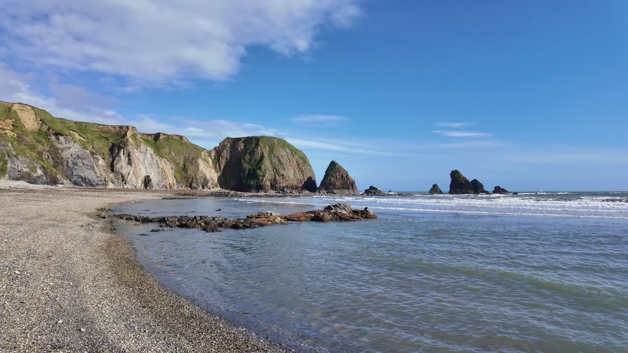 кристально чистая вода нежные волны на песчаном пляже с морскими скалами и голубое небо с пухлыми белыми облаками яркий весенний день медное побережье уотерфорд ирландия