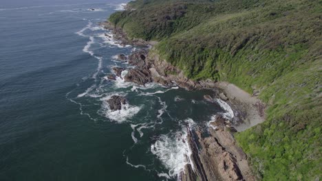 olas espumosas salpicando en acantilados verdes rocosos en forster, australia - toma aérea de drones