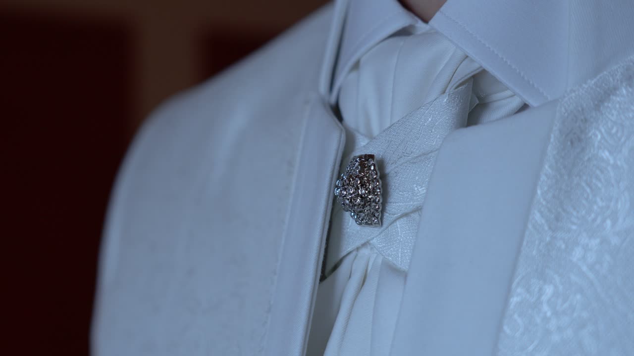 Close up of a textured white tie with an ornate silver brooch, showcasing fine details