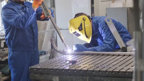 man with assistant wearing mask welding in a workshop. metal workers use manual labor. skilled welder. welder is welding the stainless steel pipes in the factory. welder industrial part in factory.