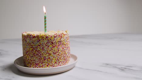 Studio-Shot-Birthday-Cake-Covered-With-Decorations-And-Single-Lit-Candle