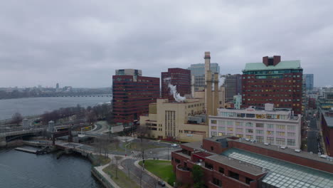 Slide-and-pan-shot-of-factory-or-heating-station-with-chimneys-on-riverbank.-Buildings-in-urban-borough.-Boston,-USA