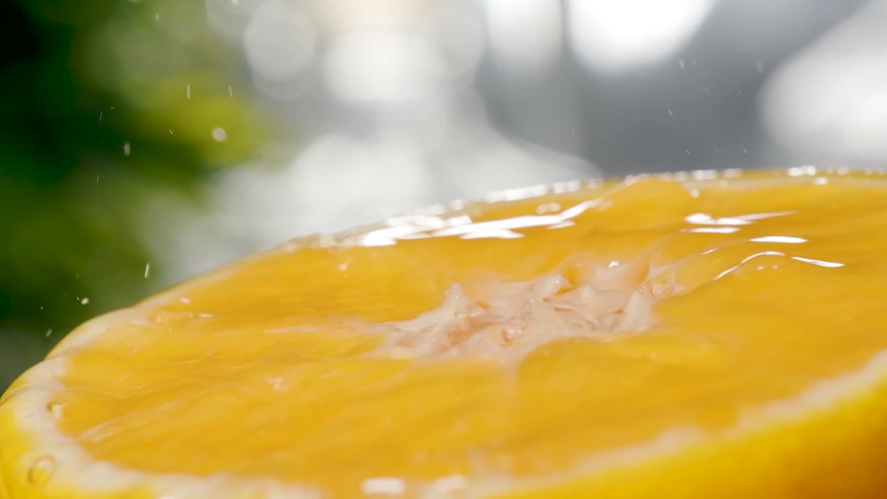 Ripresa macro estrema di acqua fresca che cade e schizza su una superficie mezza arancione, al rallentatore