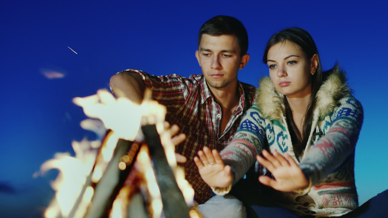 해변 모닥불에 앉아 사랑스러운 젊은 부부는 불 로맨스와 젊음으로 따뜻한 손