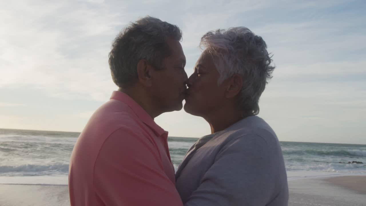 Ritratto di felice coppia anziana ispanica che si bacia sulla spiaggia al tramonto
