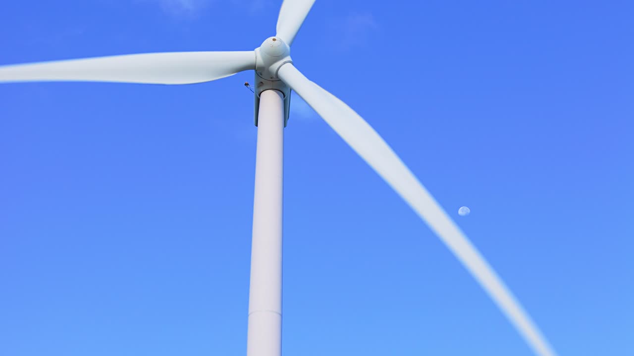 파란 하늘에서 달이 뜨면서 회전하는 풍력 터빈 블레이드 주위의 도