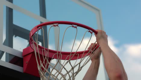 man dunking on a new basketball net and holding onto the ball rim after he makes the dunk