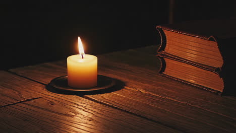candle and old books on a wooden table at night