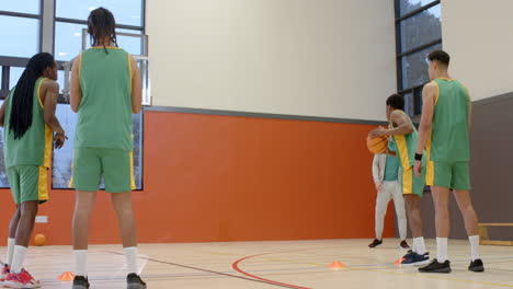 multiracial male basketball players with coach in gym, running with ball and throwing into basket