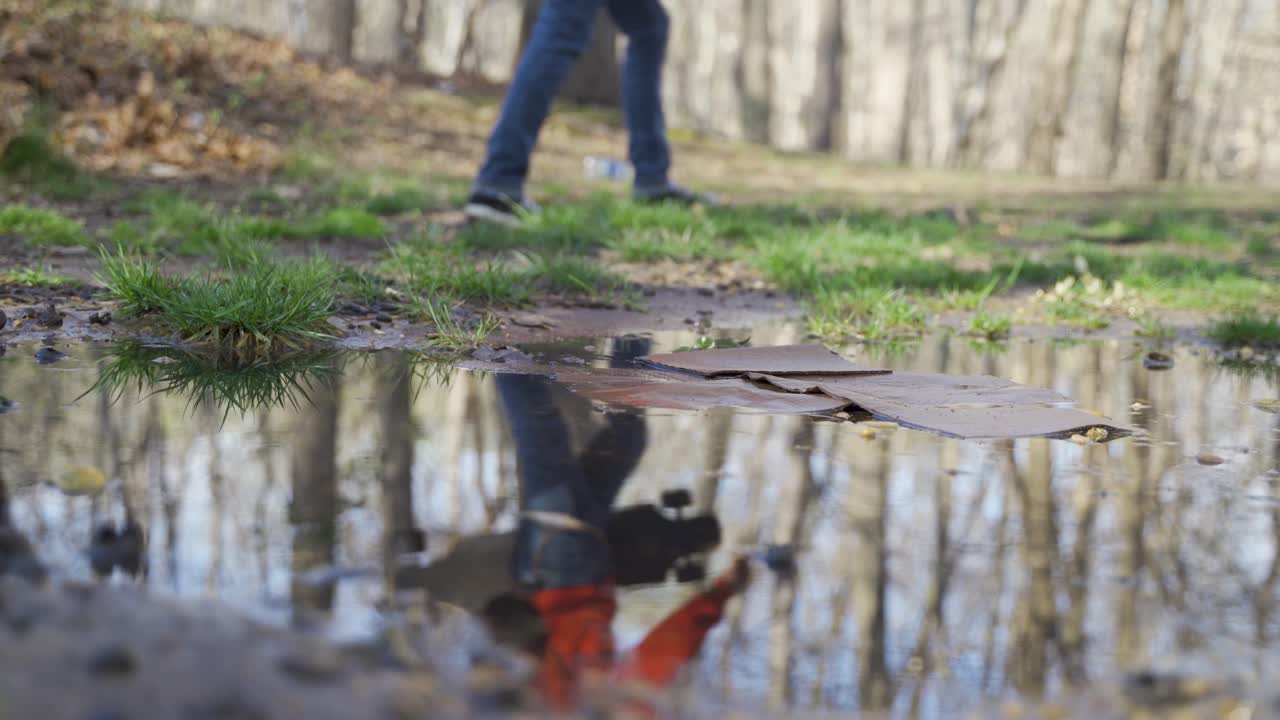 People Walking Past a Puddle with Cardboard Reflection in a Park
