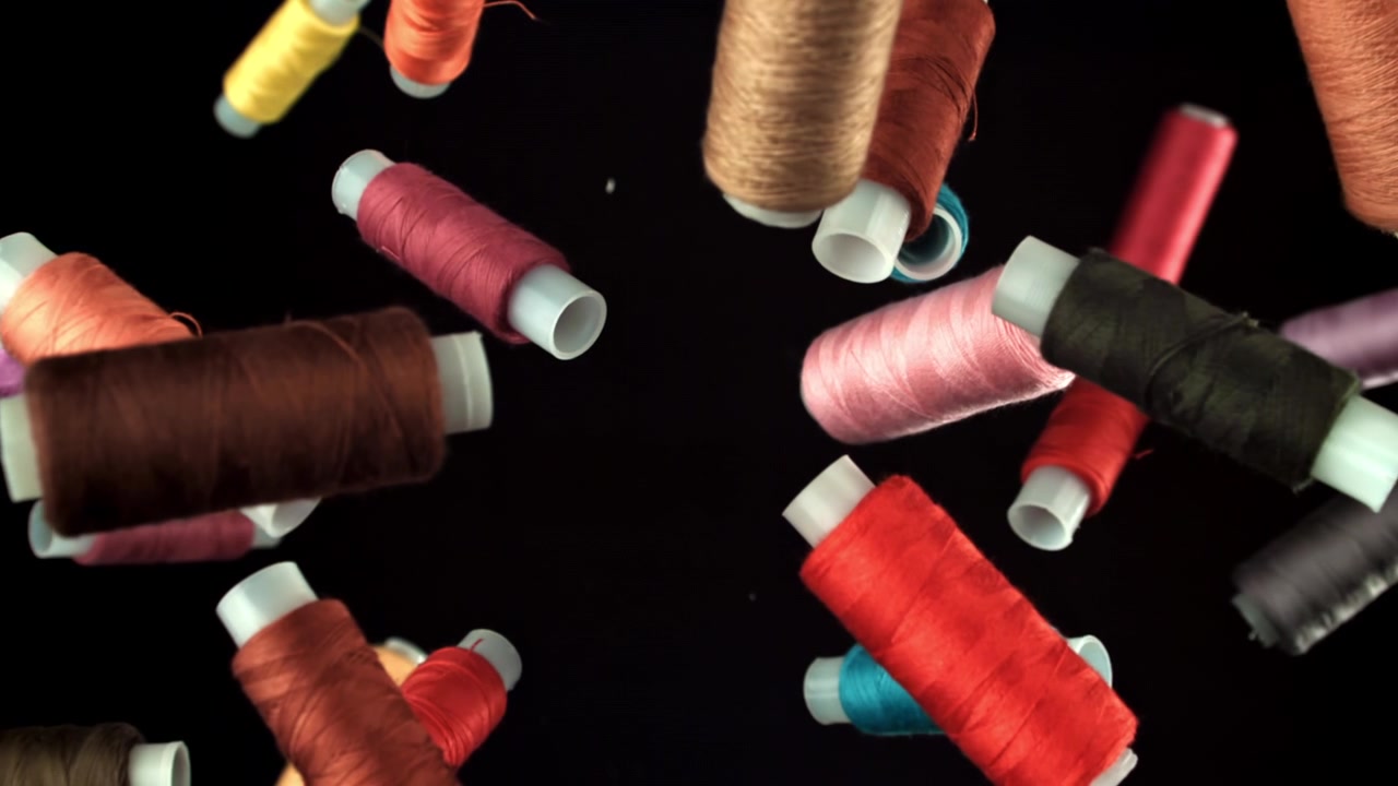 Colorful Sewing Threads Falling in Slow Motion Against Black Background