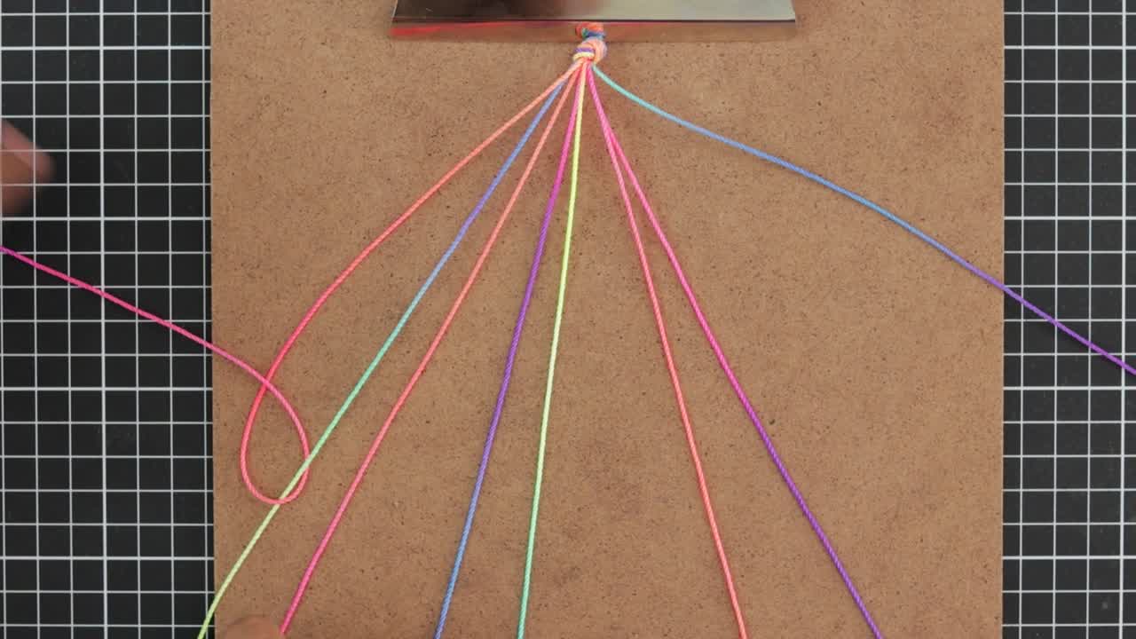 손은 다채로운 무지개 마크라메 팔를 여러 개의 활기찬 줄을 사용하여 짜고 있습니다.