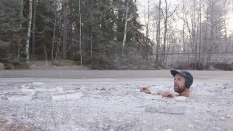 a rugged bearded ice bather sits in his ice hole in a swedish lake