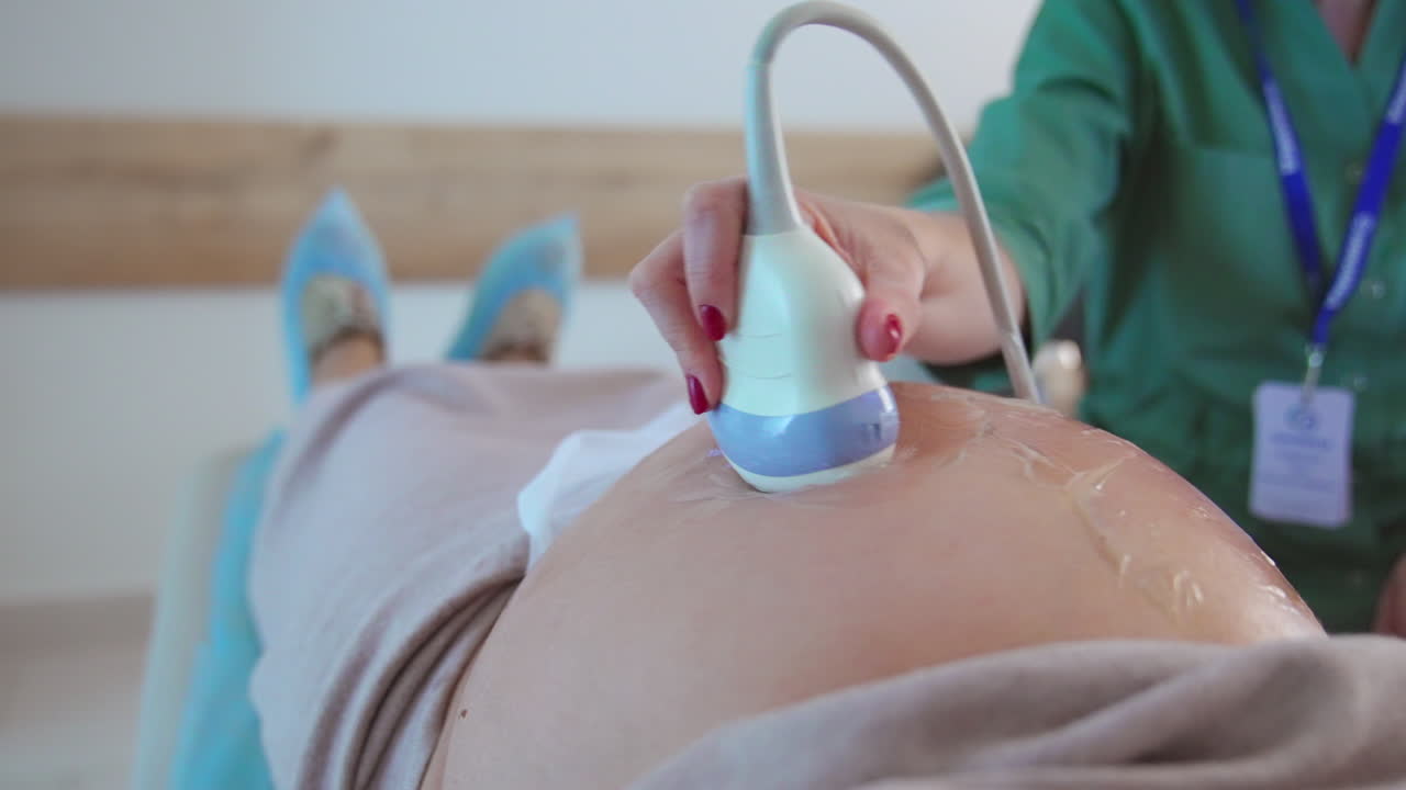 Pregnant woman with big stomach at doctor's examination. Doctor uses ultrasound device to see the baby development. Close up.