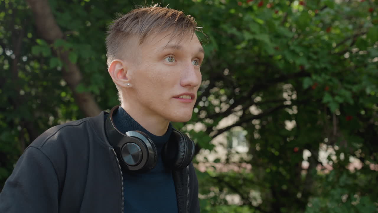 young man with headphones in rain, wet hair and raindrops on skin, candid outdoor portrait in leafy park, subtle cinematic lighting, shifting gaze from downward reflection to hopeful upward look