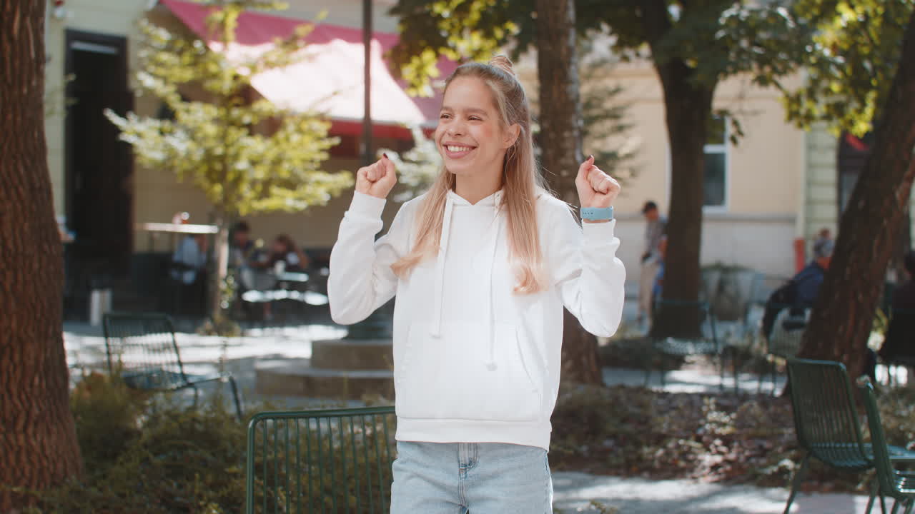 놀란 모습을 보이는 젊은 여성이 시내 거리에 서서 갑작스러운 승리에 충격을 받아 주먹을 고 있습니다.