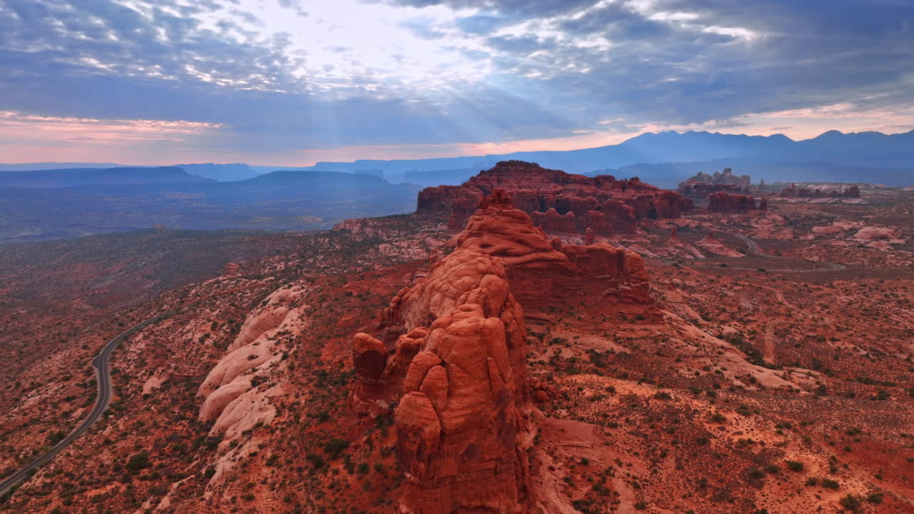 Approaching rounded orange rocks in the Arches National Park in Utah, USA. Setting sun sends the rays through the clouds covering the sky. Aerial perspective