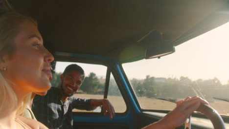 group of smiling friends on road trip driving in cab of pick up truck