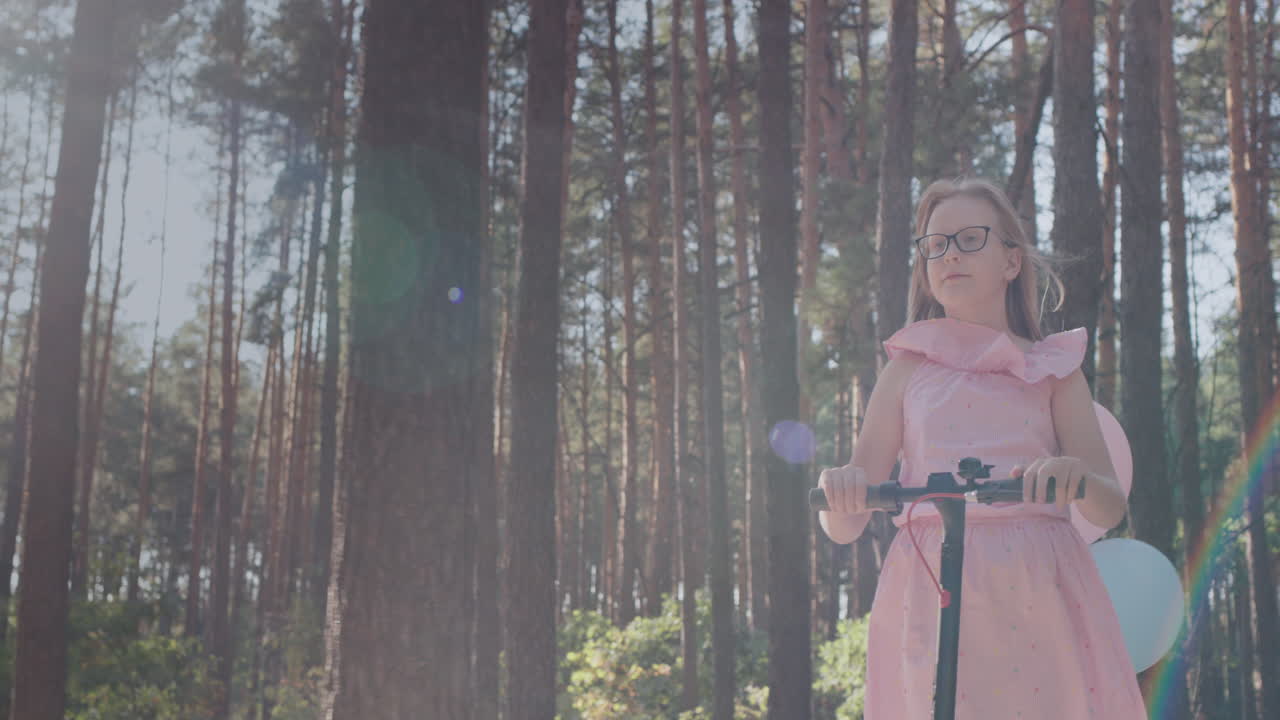 девочка в розовом платье катается на самокате в парке