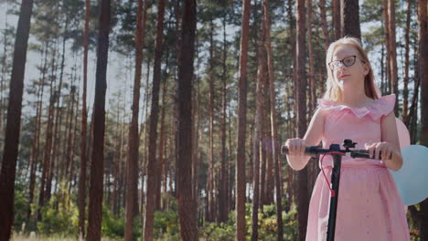 a girl in a pink dress rides a scooter in the park