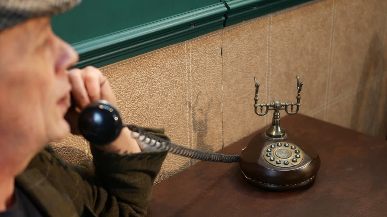 A man wearing a flat cap lifting the receiver of a vintage rotary phone and answering. The old-fashioned telephone adds a nostalgic touch to the scene, evoking a sense of timelessness