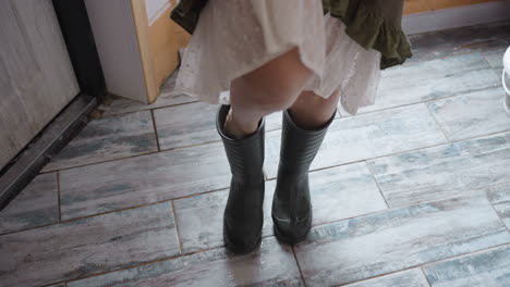 nature enthusiast wearing sturdy boots stepping outside through wooden doorway into snowy landscape, dress ruffles brushing tiled threshold, footprints in fresh powder beyond door