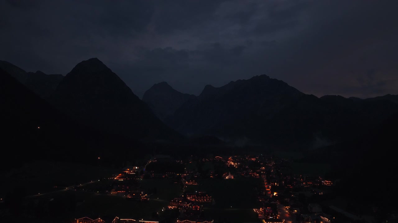 Vista aerea inclinata verso l'alto sopra la città illuminata sul lago Achensee e le montagne alpine, Austria