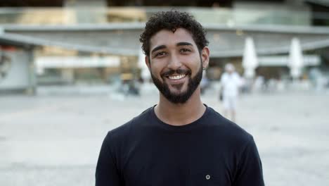 Smiling-curly-guy-with-piercing-standing-on-street