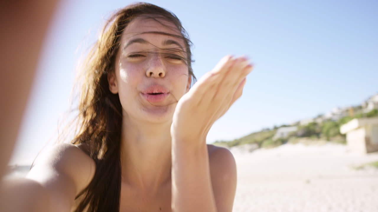 hermosa joven tomando una selfie en la playa al atardecer soplando un beso