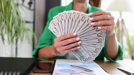 close-up of a woman's hands holding a fan of us 100 dollar bills
