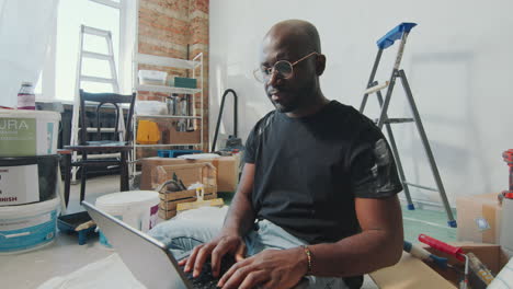 African American Man Using Laptop in Living Room under Renovation
