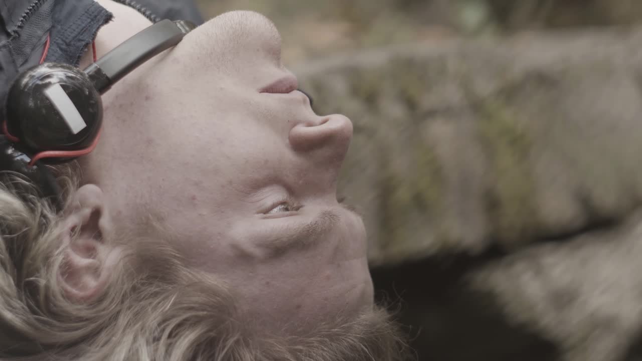 Man som ligger ner i en skog med hörlurar