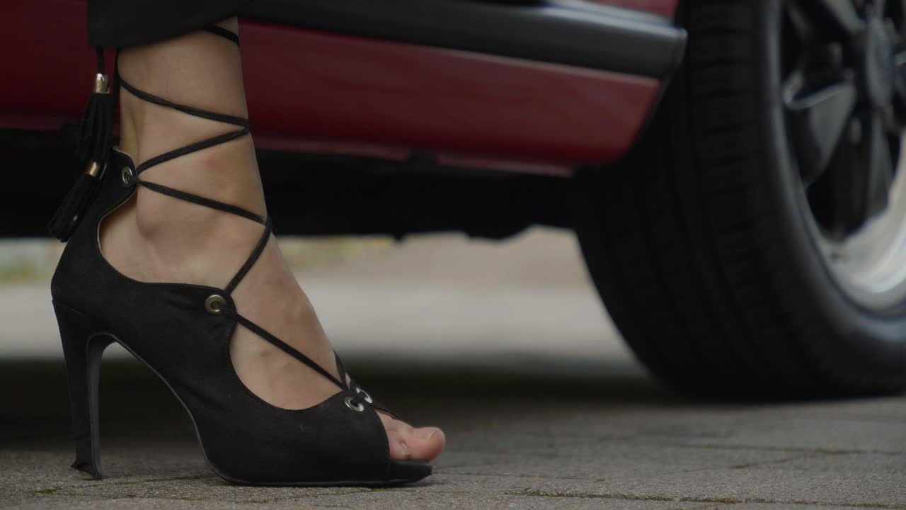plano bajo de los pies de una mujer saliendo de un auto con tacones altos negros, auto rojo y muy a la moda y sexy, en cámara lenta