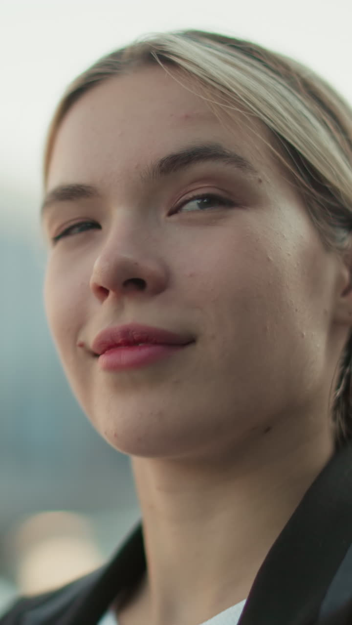 Close up of professional lady in black suit smiling slightly with confident expression and blurred background of modern building and cars in urban environment