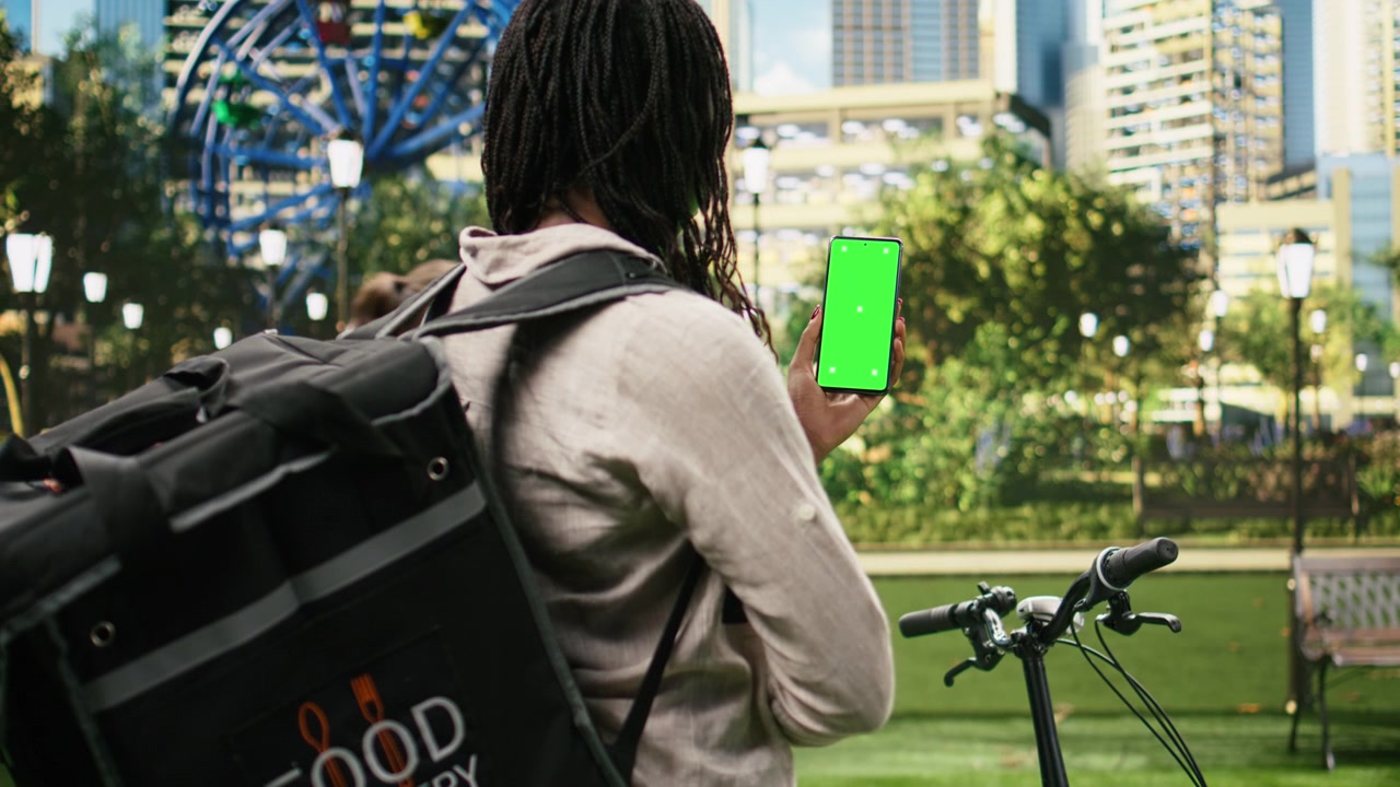 Vertical green screen smartphone mockup held by delivery courier in urban park