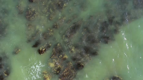 Rising-top-down-aerial-view-of-the-tide-rolling-in-over-rocks-at-Brighton-Beach,-UK