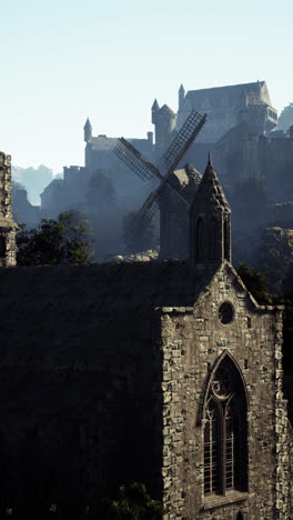 a stone church with windmill and castle in distance