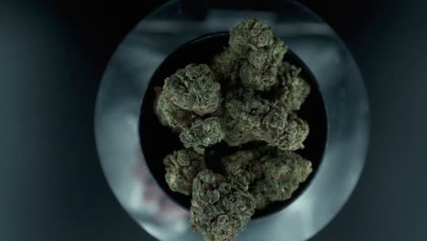 grayish green dried marijuana buds view from above, pile of dried marijuana plants in a shiny bowl, trichomes strains, on a reflecting rotating stand, studio lights, slow motion 120 fps zoom in