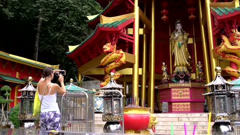 a woman is photographing a statue of a deity in a buddhist temple