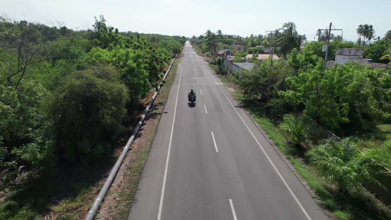Motorcycle rides on open road through lush green landscape, sunny day