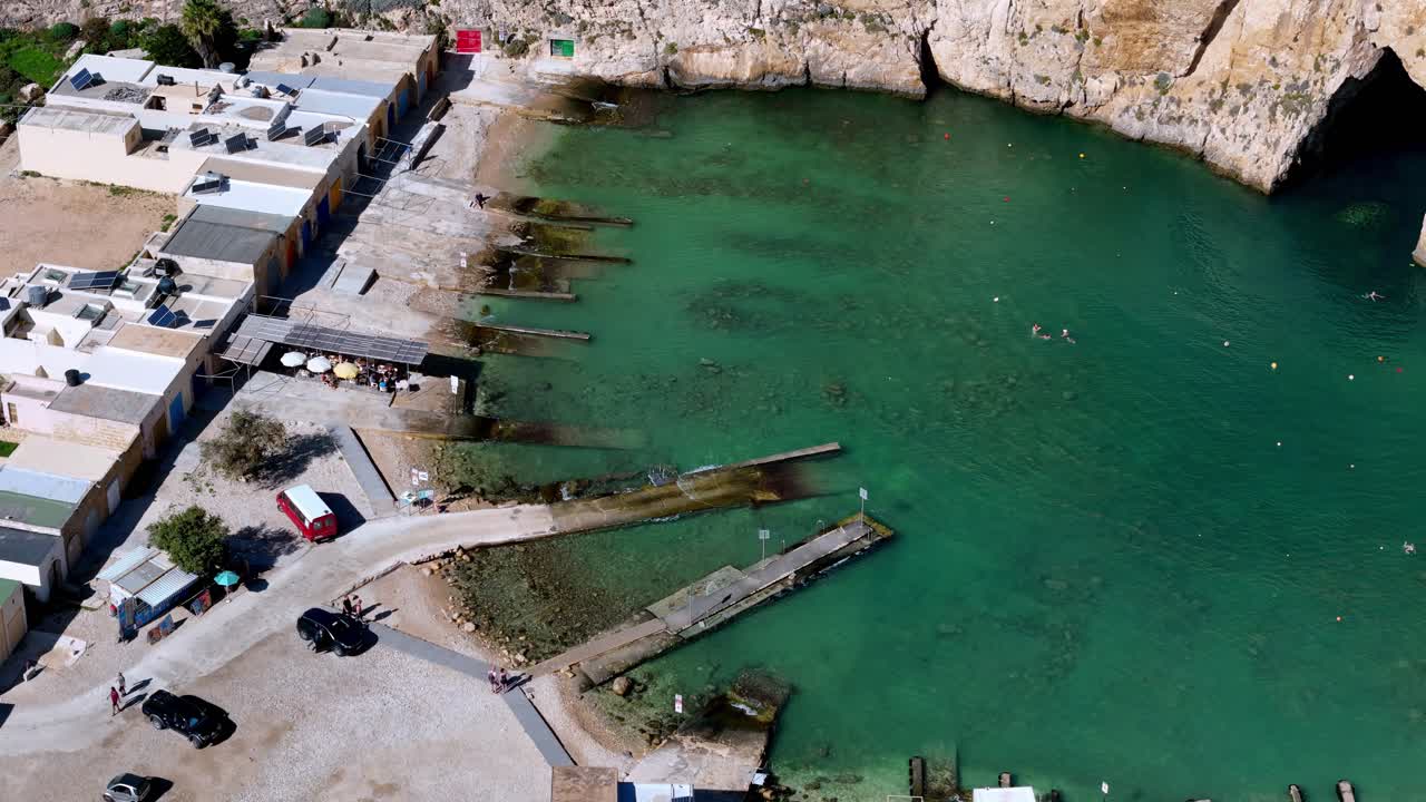 Una ripresa aerea con drone cattura la tranquilla storia della vita estiva a Dwejra Inland Sea a Gozo, Malta, sotto un cielo sereno e soleggiato, mettendo in mostra le vivaci acque turchesi e gli scivoli in pietra calcarea