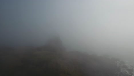 aerial: cutting through the oregon fog our drone begins to reveal a rock formation