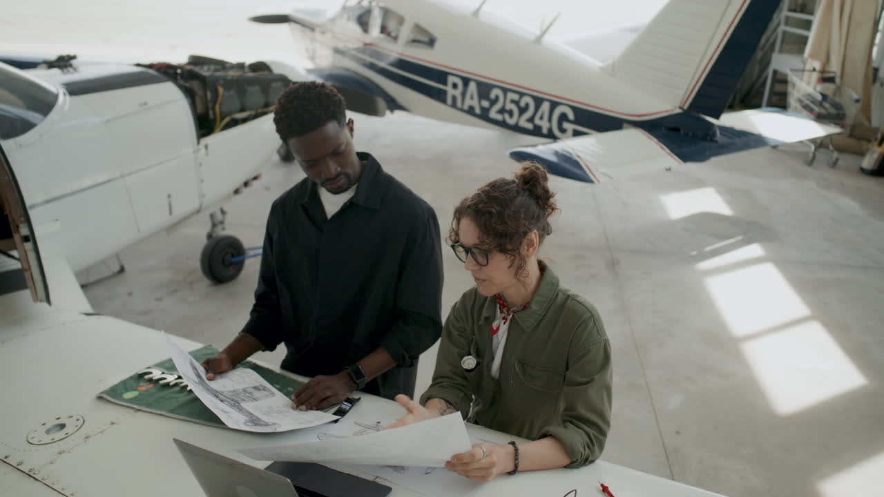 Avionics Mechanic Discussing Aircraft Schematics with Colleague in Hangar