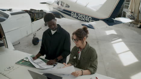 avionics mechanic discussing aircraft schematics with colleague in hangar