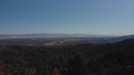 A-drone-takes-off-in-blue-skies-near-the-mountains-and-forests-of-the-California-Peninsula-opening-up-a-100-mile-view