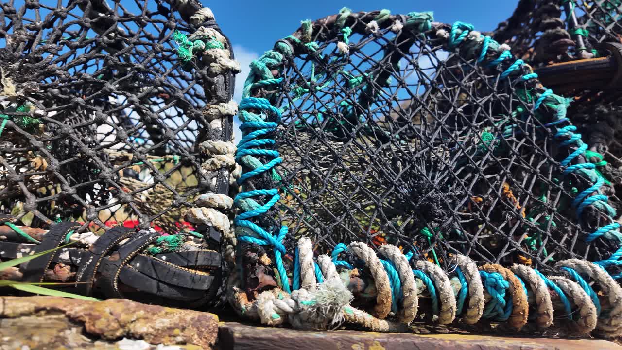Used crab traps with netting and rope sitting on a stone wall under a blue sky
