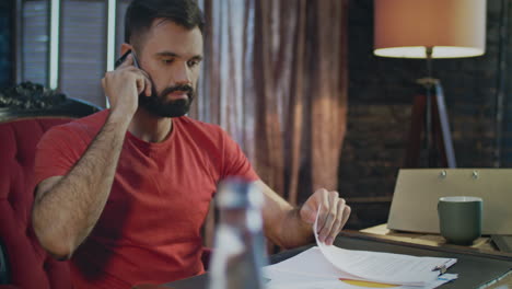 Young-business-man-hearing-bad-news-talking-on-phone-in-home-office-at-evening